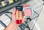 person holding maybelline foundation and blush over a cart