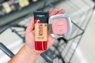 person holding maybelline foundation and blush over a cart