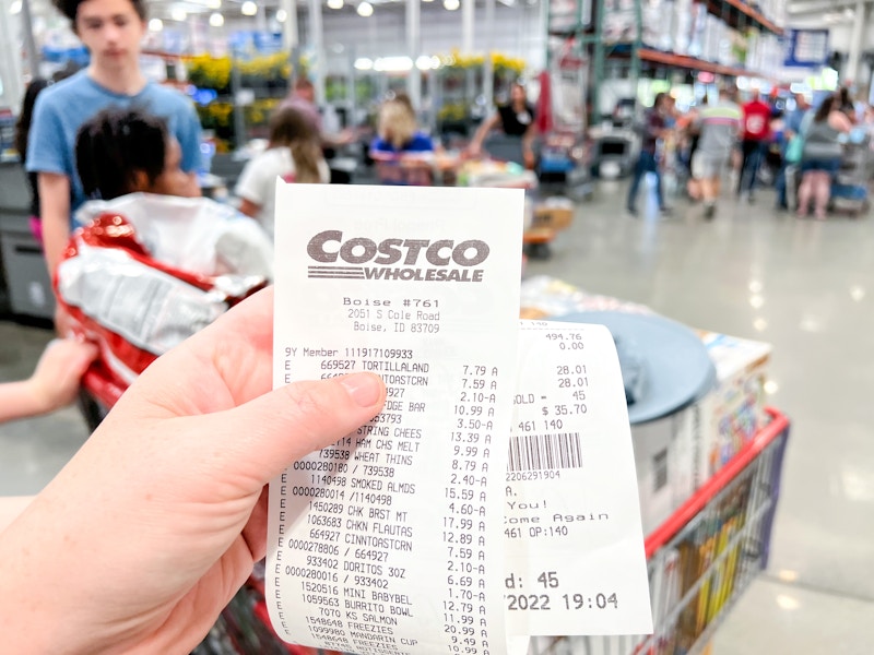 A person holding a long Costco receipt in front of a shopping basket.