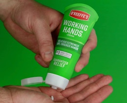 a person squeezing lotion from a green tube into their hands