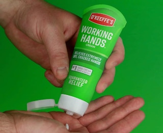 a person squeezing lotion from a green tube into their hands