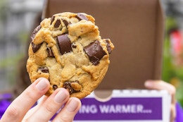 A person holding an Insomnia Chocolate Chunk cookie in front of an Insomnia Cookies to-go box.