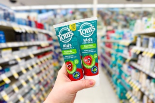 person holding 2 tom's of maine kids toothpastes in an aisle