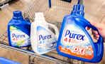 hand holding a bottle of purex detergent with two bottles in walmart cart