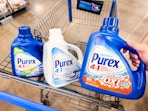 hand holding a bottle of purex detergent with two bottles in walmart cart
