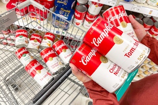 a person holding cans of soup to put into shopping cart