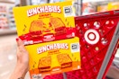 hand holding 2 lunchables in front of a target cart