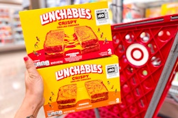hand holding 2 lunchables in front of a target cart