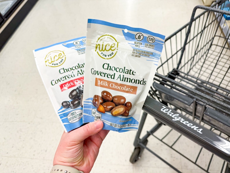 person holding 2 bags of chocolate covered almonds over a walgreens cart