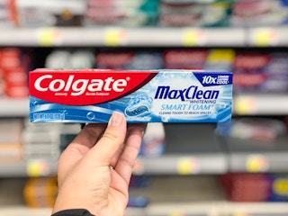 hand holding box of Colgate toothpaste in front of Walmart shelf