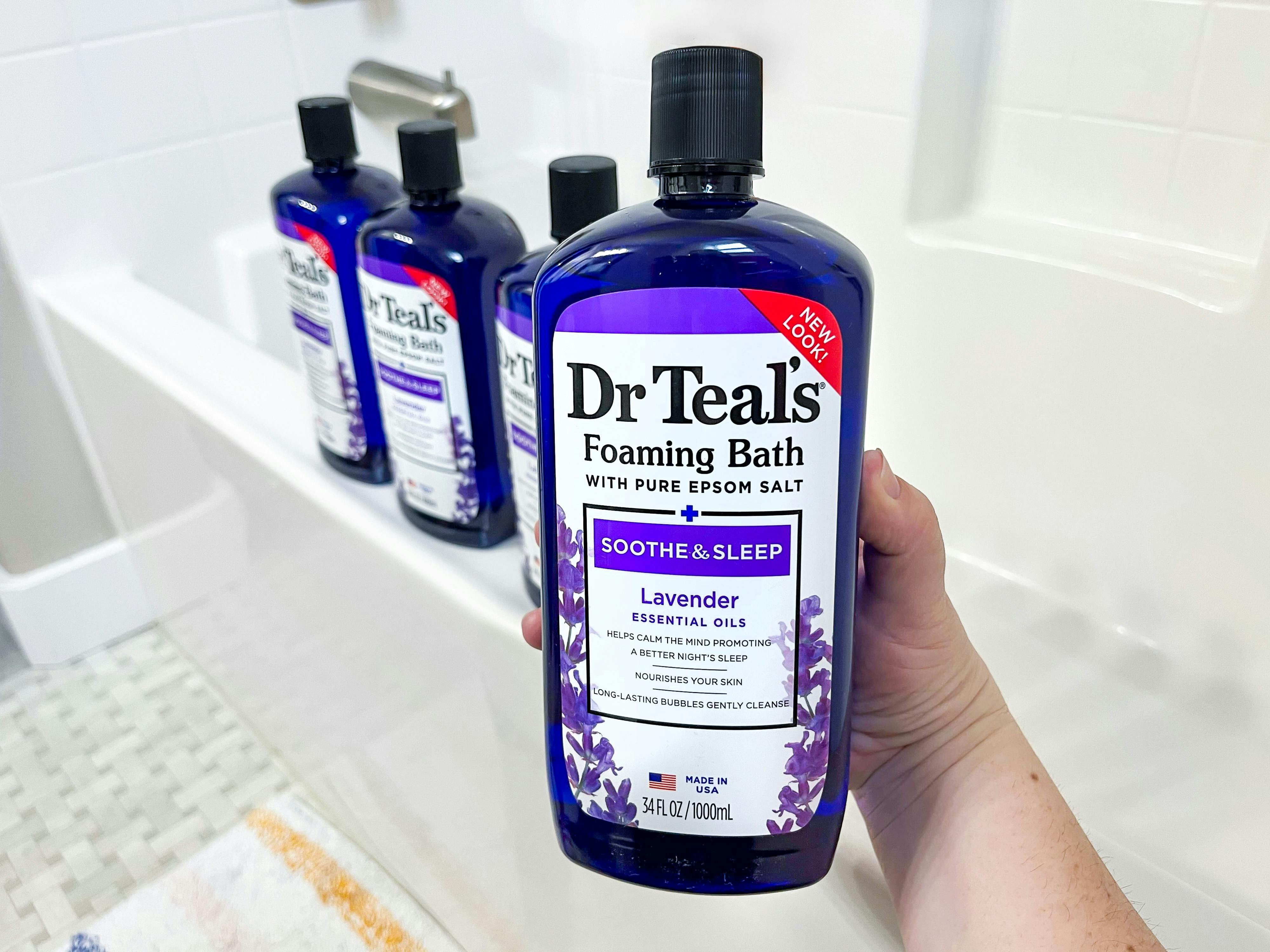 a hand holding a blue bottle in front of a tub with three blue bottles