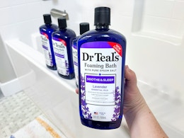 a hand holding a blue bottle in front of a tub with three blue bottles