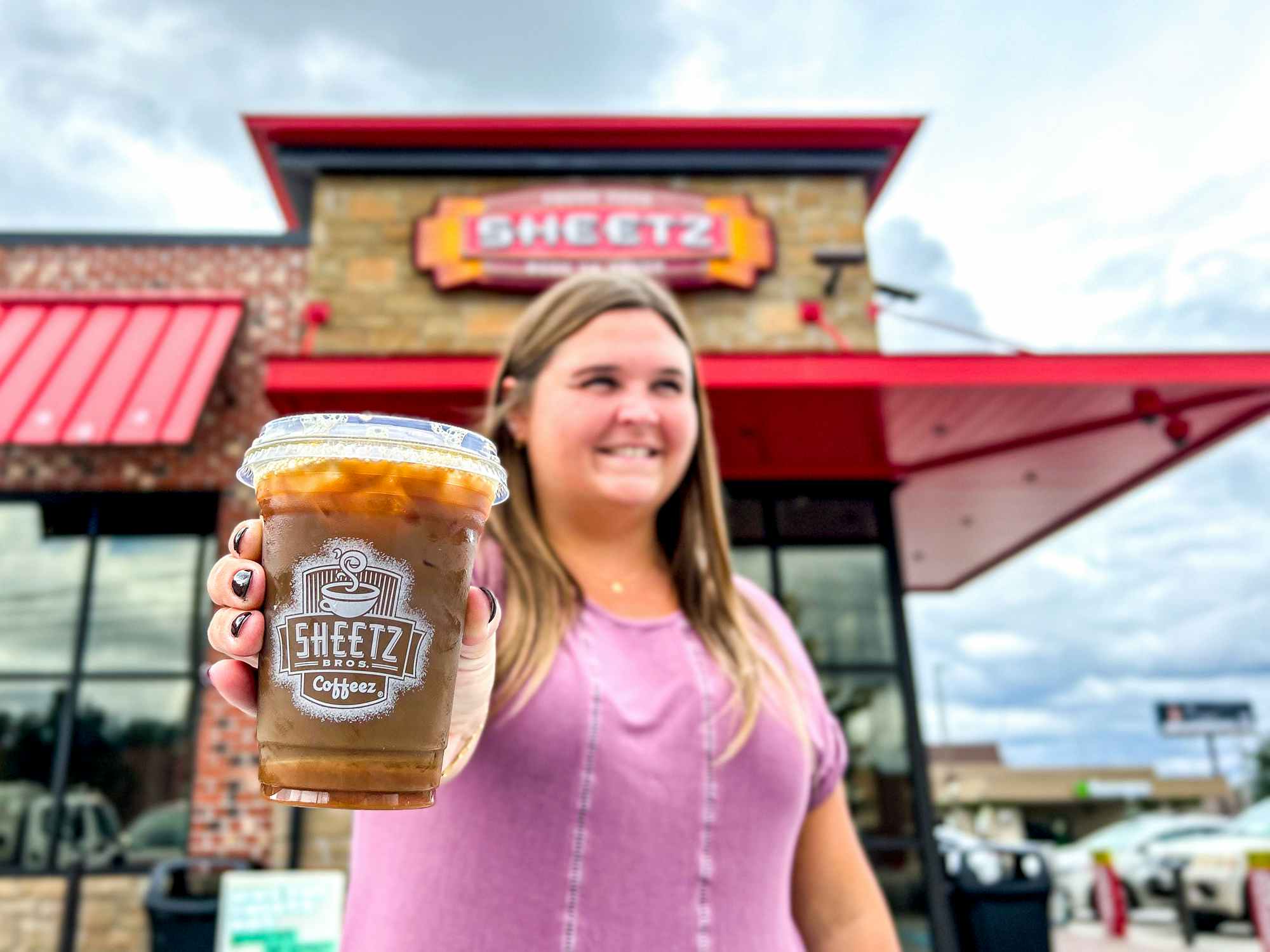 a person standing outside of sheetz with a cup of coffee smiling