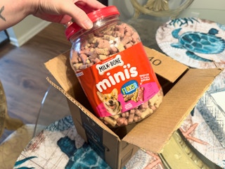 Someone taking a tub of Milkbone Mini dog treats out of an Amazon box