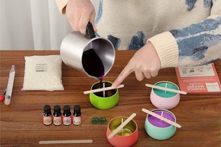 A woman pours hot wax into a candle with a kit spread out around her