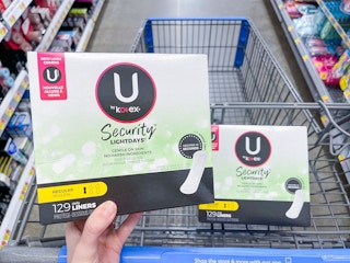 A U by Kotex liners package held out by hand in front of another U by Kotex liners sitting in a store cart.