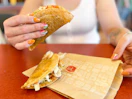 a jack in the box taco being held up with another laying on the wrapper sitting on the table