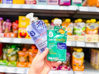 hand holding two pouches of cerebelly baby food puree in walmart aisle
