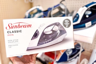 person holding a box with a sunbeam iron in front of a display of irons