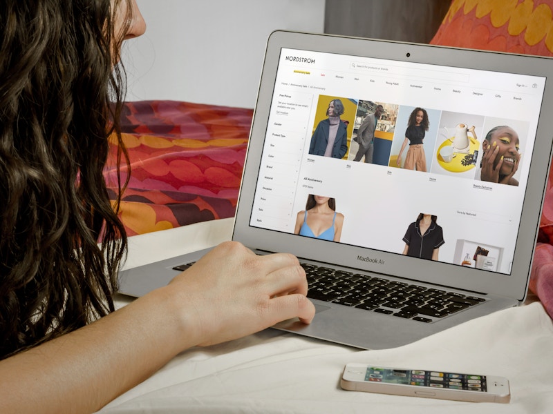 A person laying on a bed and shopping the Nordstrom online anniversary sale on a laptop.