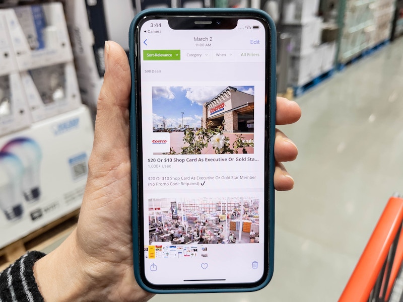 A person holding a cell phone inside Costco, with a Groupon deal for a Costco membership displayed on the phone