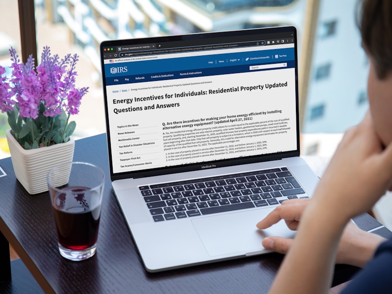 A person using a laptop displaying the IRS website's page for Energy Incentives for Individuals: Residential Property Updated Questions ...