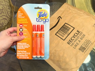 Someone holding a three pack of Tide to go pens next to an Amazon envelope