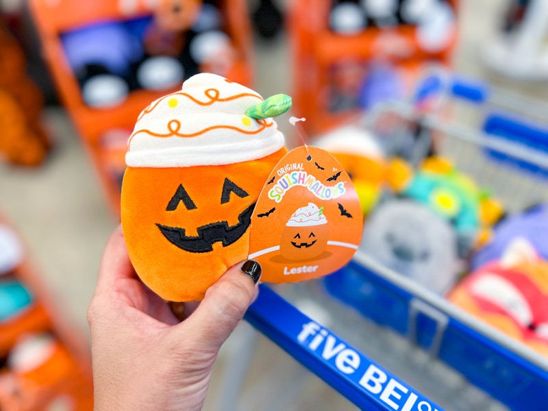 a person holding a squishmellow pumpkin in front of a five below cart