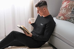 Man sitting up against a couch drinking a cup of coffee wearing the Xtreme Heat Compression Pants & Shirt in black