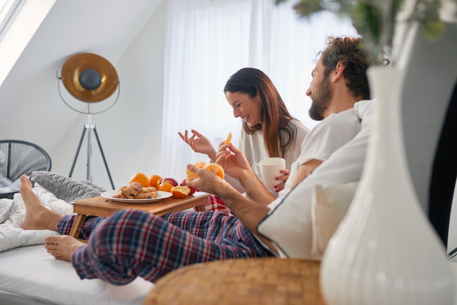 A couple sitting in bed with a tray of breakfast laughing together