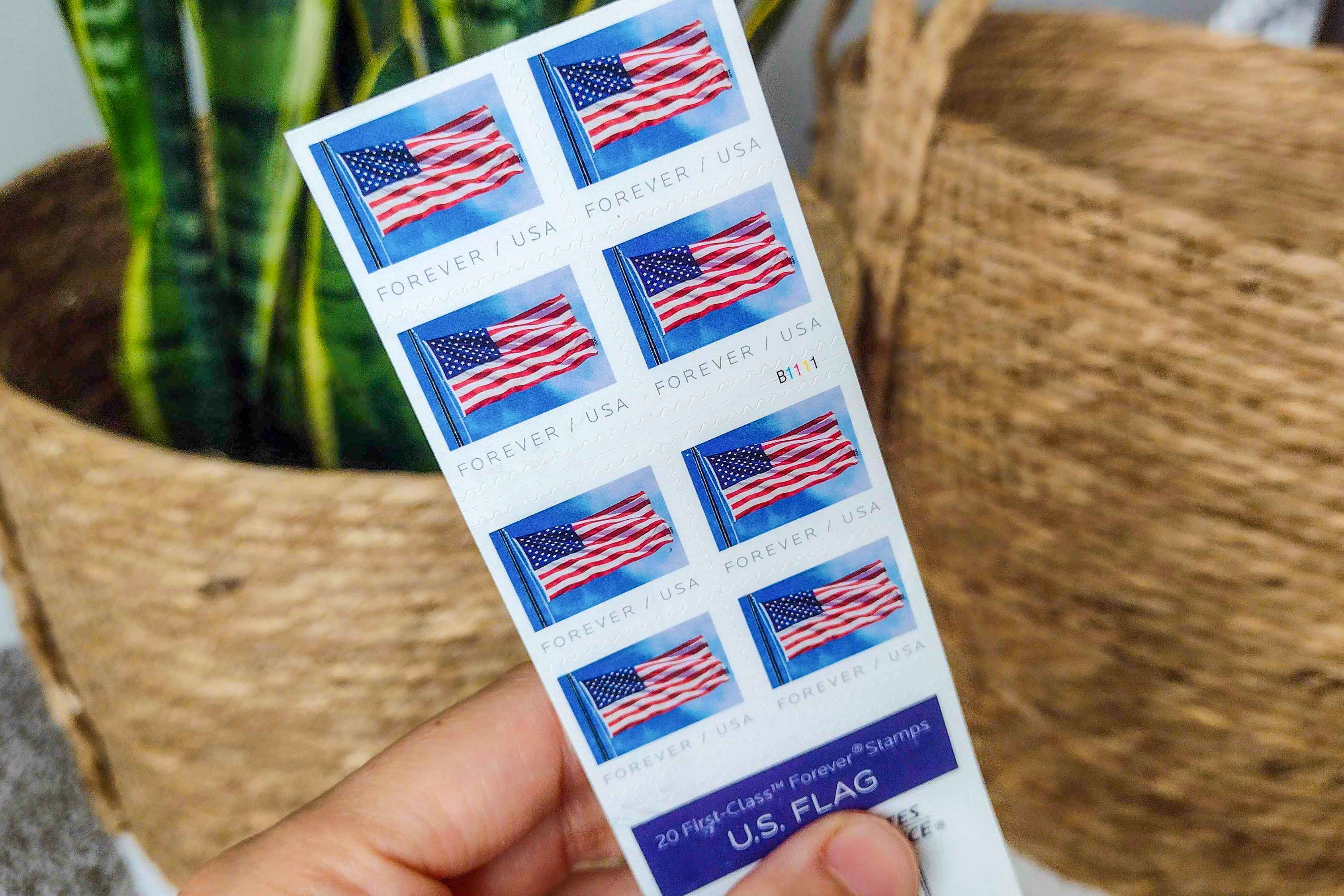 A person's hand holding some American flag Forever postage stamps.