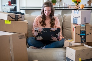 A woman sitting on a couch with a laptop computer one her lap, surrounded by amazon delivery boxes.