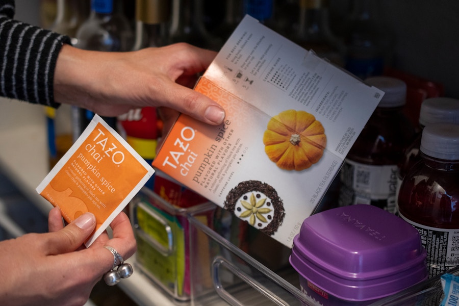 A tea bag packet being pulled from a box of tea off a dark pantry shelf