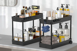 Two dark brown under sink organizers with two tiers each. They have two wheels in the back and hooks on two sides.