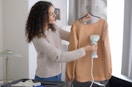 a woman using a conair garment steamer on a blouse 