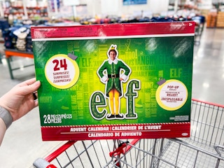 person holding an elf advent calendar over a costco cart