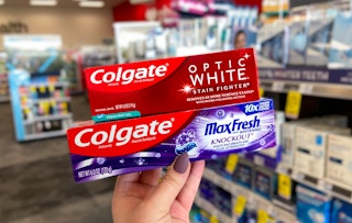 A person's hand holding up two boxes of Colgate toothpaste.