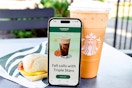 a phone propped up against an iced coffee and breakfast sandwich from starbucks 