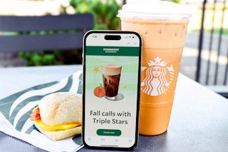 a phone propped up against an iced coffee and breakfast sandwich from starbucks 