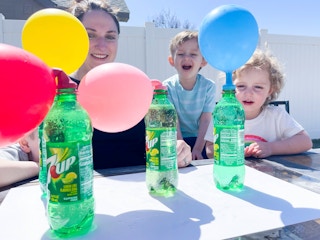 Children and an adult watching in excitement as balloons are inflated on top of 7Up bottles
