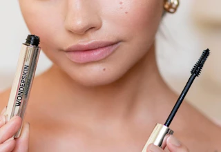 a person holding a tube of mascara and it's wand