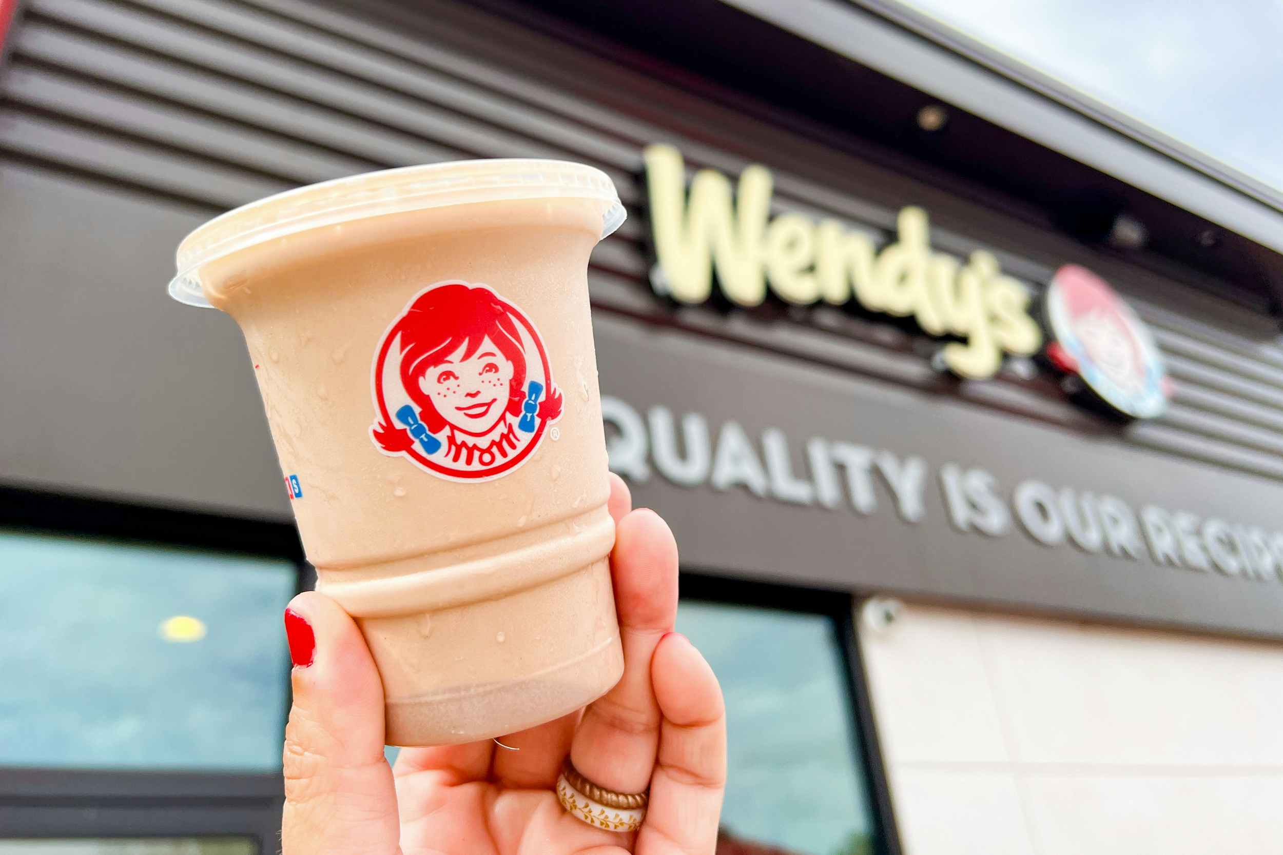 a small wendy's frosty being held up in front of a wendy's sign