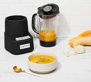 A blender filled with puree and soup in a bowl on a table