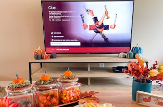 the movie clue on tv with coffee table filled with fall snacks, decor and a remote