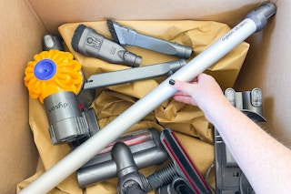 a person's hands grabbing a dyson vacuum together from parts in a box on the ground