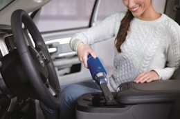 a woman using a Bissell Handheld vacuum in a car