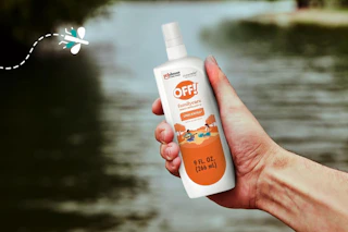 hand holding off bug spary over lake