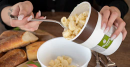 person spooning out macaroni and cheese from panera family box container