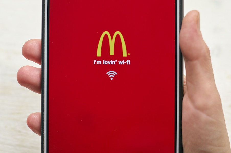 A person's hand holding a phone with the McDonald's app open showing the golden arches logo and reads "I'm lovin' wi-fi