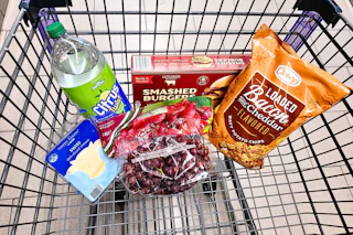 soda, burgers, chips, sliced cheese, and grapes in a cart